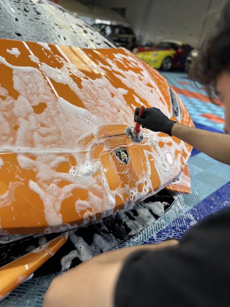 Lavage à la mousse active d’une voiture orange au centre FD, formation lavage auto pour pros en Belgique