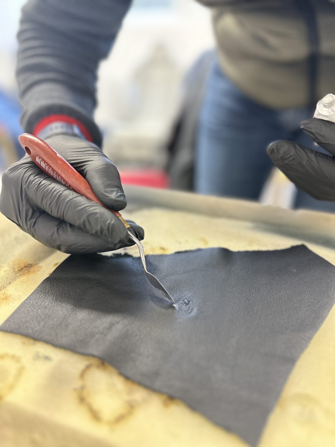 Application de mastic sur un échantillon de cuir noir, formation restauration du cuir auto en Belgique