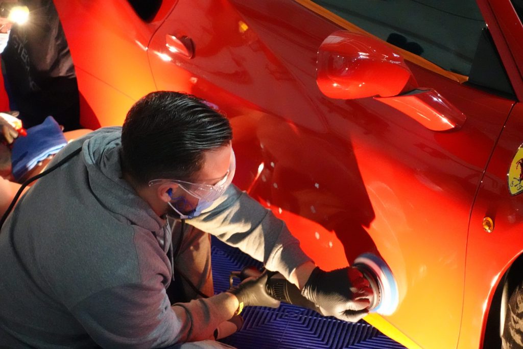 Formateur polissant une carrosserie orange à la machine, formation polissage automobile en Belgique